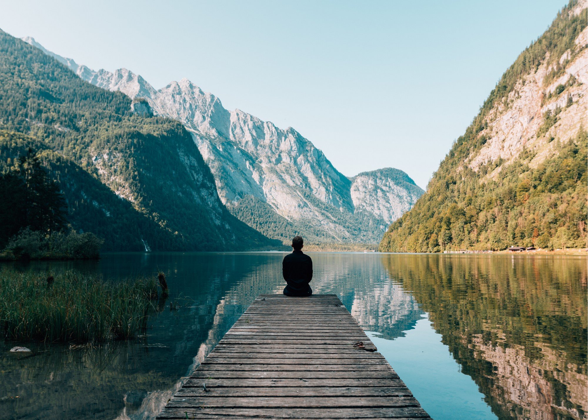 Person meditating on a dock overlooking a mountain lake